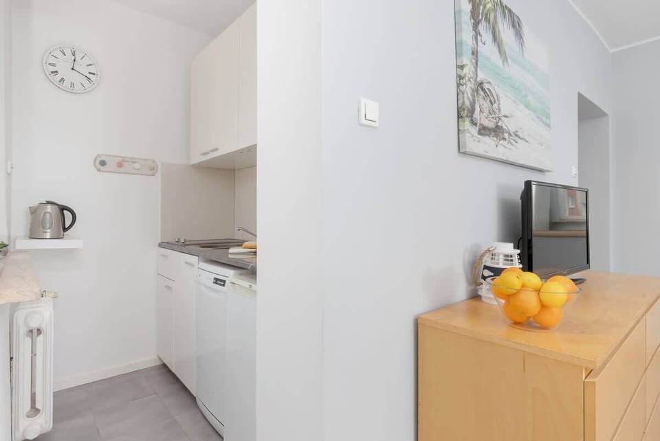 A compact, modern kitchen with a white electric stove and slim cabinetry, lit by a window above the sink.

