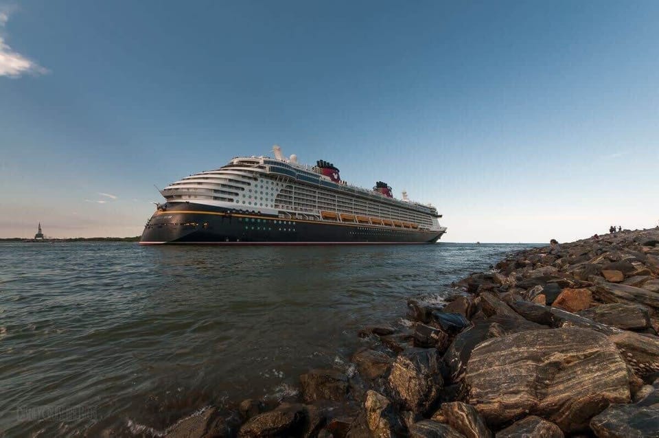 View of a large cruise ship sailing near a rocky shoreline under a clear sky