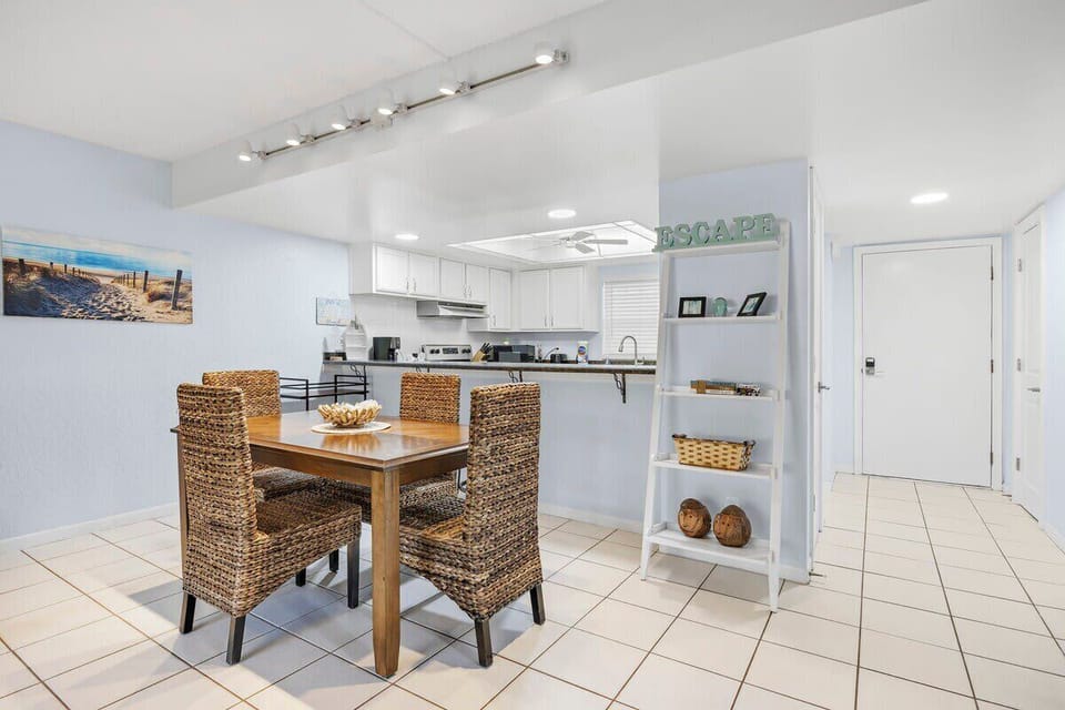 Dining area with woven chairs adjacent to a bright kitchen and entryway