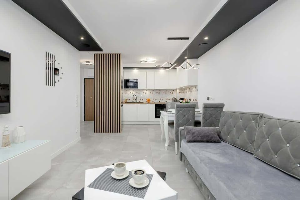 Spacious living area with a gray couch, white floors, and TV mounted on the wall.
