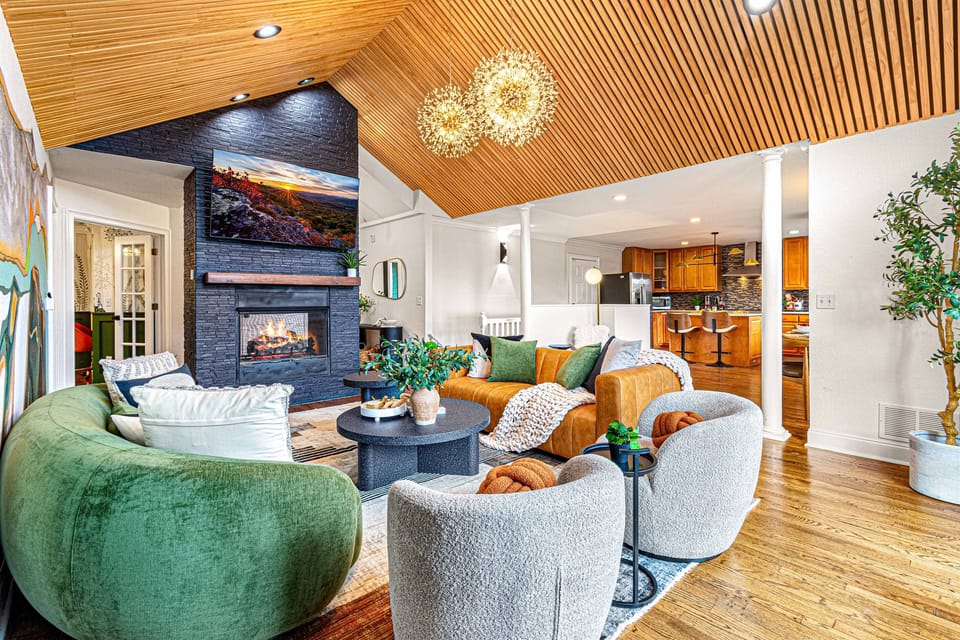 Gather in this stunning living room with a vaulted wood ceiling, cozy fireplace, and modern decor. A perfect spot to relax and enjoy the warmth and ambiance.