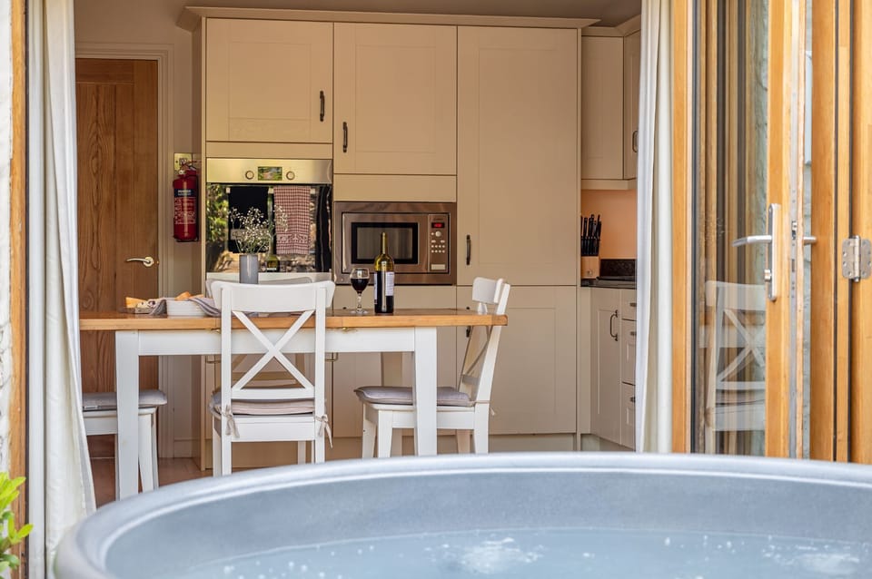 Bright kitchen and dining area at Woodcroft Cottage with modern fittings, wooden table and doors opening to hot tub patio.