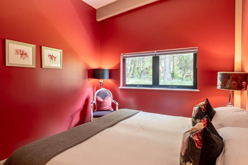 Boutique style bedroom with red feature wall, seating area and garden views at Percy lodge, Brompton Lakes.