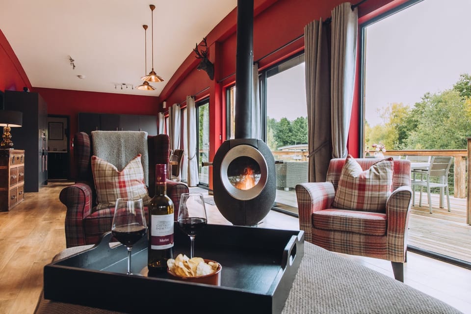 Seating area at Isabella with armchairs, a coffee table with drinks, a wood-burning stove, and large doors opening onto the deck