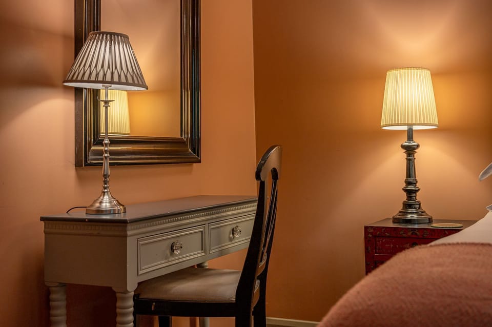 Dressing table at Isabella with a chair, mirror, and lamp beside the bed.