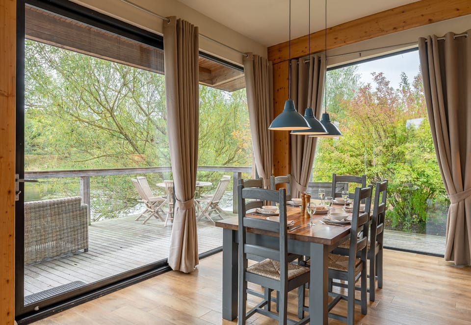 Dining area in William lodge at Brompton Lakes with large sliding doors opening onto private lakeside decking and woodland views.