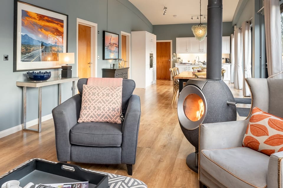 Open-plan living area with log burner, sofa, armchairs in Lola lodge at Brompton Lakes, Yorkshire.