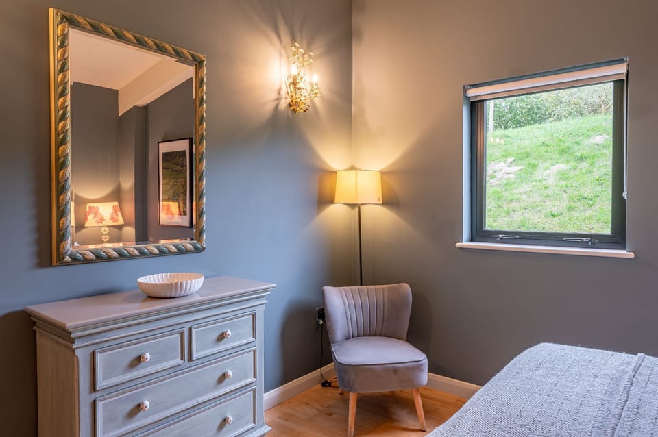 Bedroom with king-size bed, dresser, armchair and mirror in Juniper lodge, Brompton Lakes.
