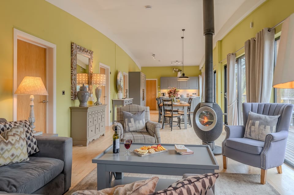 Spacious open-plan lodge interior with dining area, kitchen and wood burning stove in Louis lodge at Brompton Lakes.