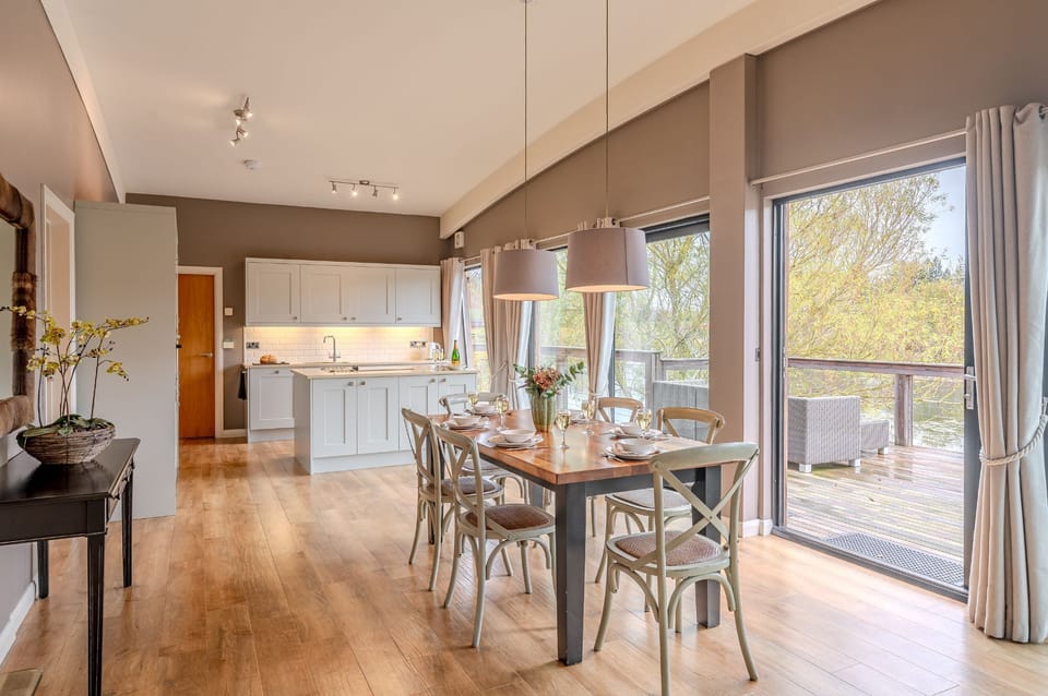 Open-plan kitchen and dining area in Flora lodge at Brompton Lakes with large table and sliding doors to private lakeside decking.