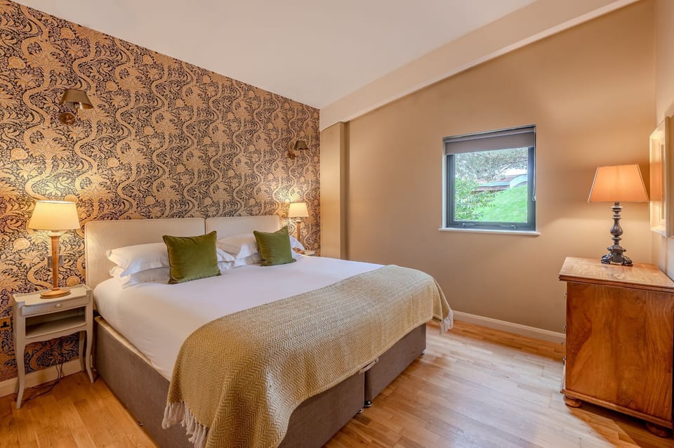 Elegant double bedroom in Flora lodge at Brompton Lakes with feature wallpaper, king-size bed and soft ambient lighting.