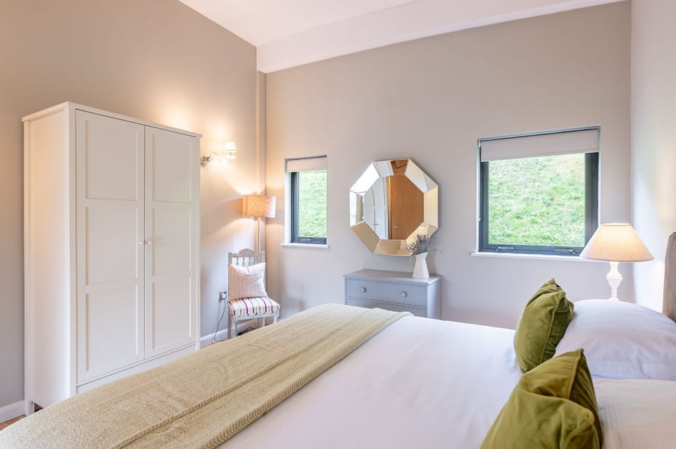 Bright bedroom in Charlie lodge at Brompton Lakes with king-size bed, dresser, mirror, wardrobe and garden views.