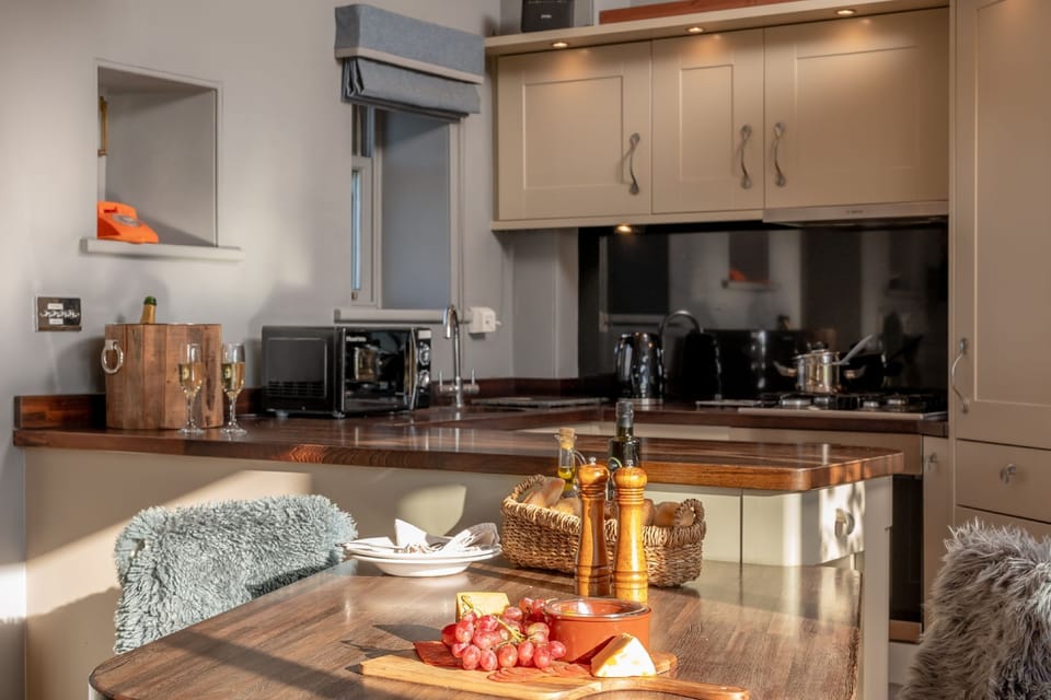Modern kitchen at Wayside Cottage with wooden worktops, breakfast bar, coffee machine, and dining table set with cheese and wine.