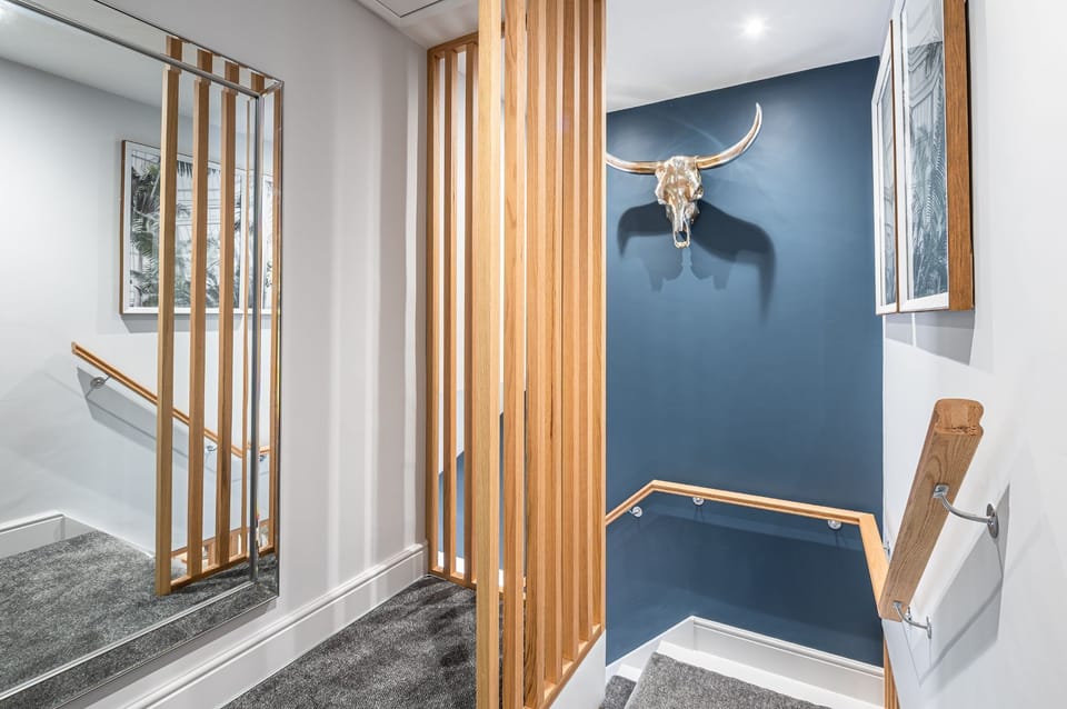 The Old Tack Room modern staircase with wooden balustrade, feature blue wall and decorative wall art.