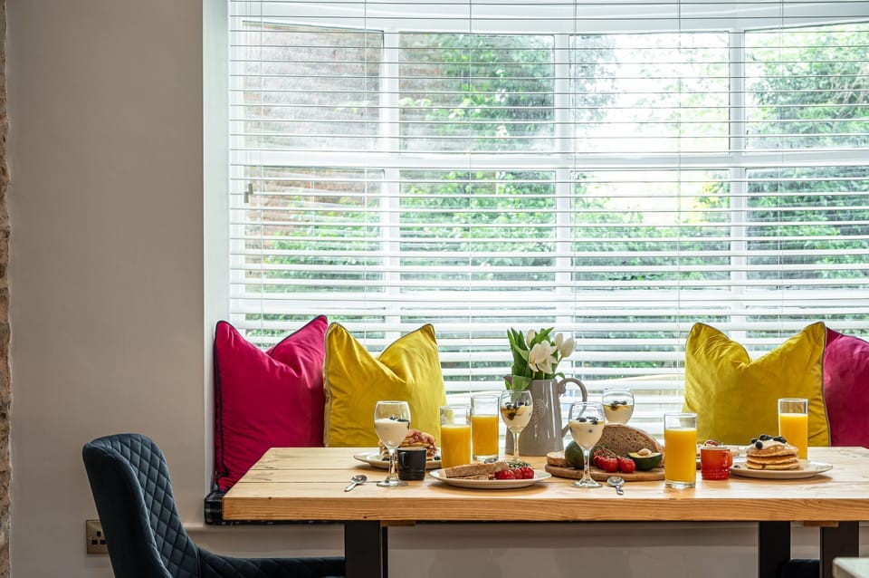 Dining area with window seat, colourful cushions and breakfast table set with fresh food and drinks in The Old Tack Room.