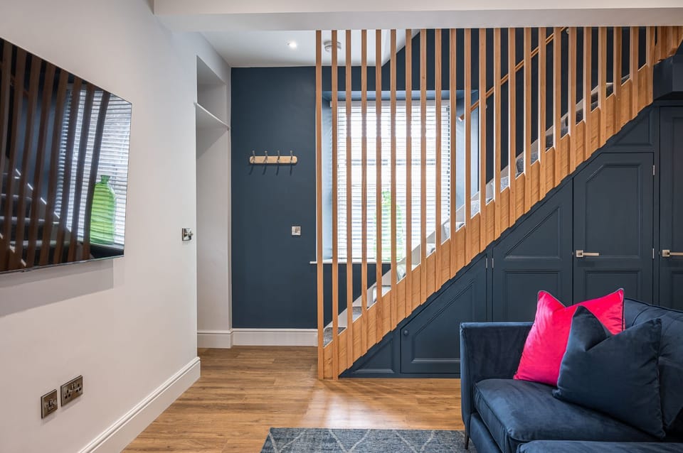 The Old Tack Room contemporary living area with navy feature wall, wooden staircase with vertical slats and cosy sofa with colourful cushions.