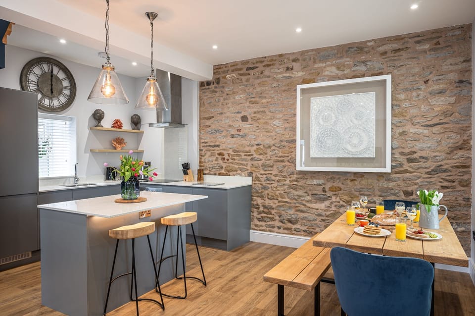 Modern kitchen with island, pendant lighting and rustic stone feature wall in The Old Tack Room.