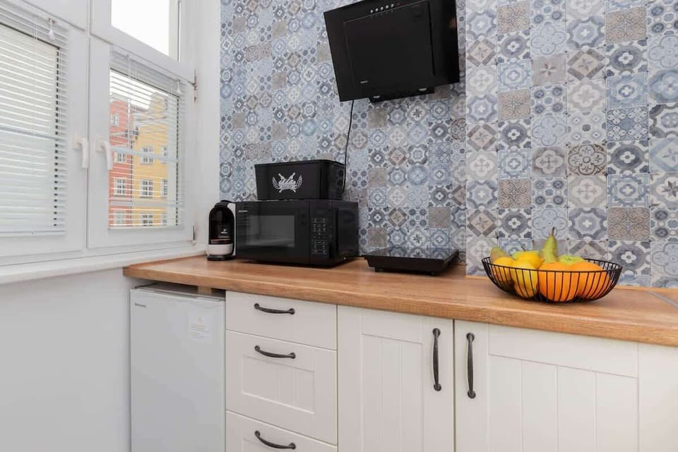 Small kitchen area with patterned tile backsplash, fruit bowl, and modern finishes.