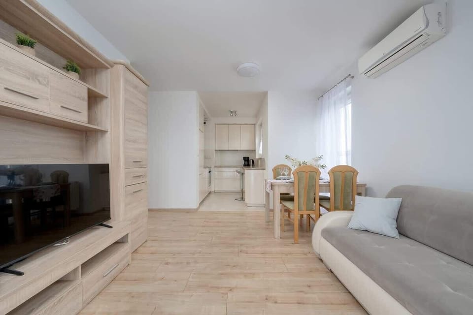 Long living room with a TV, couch, and light wooden flooring.