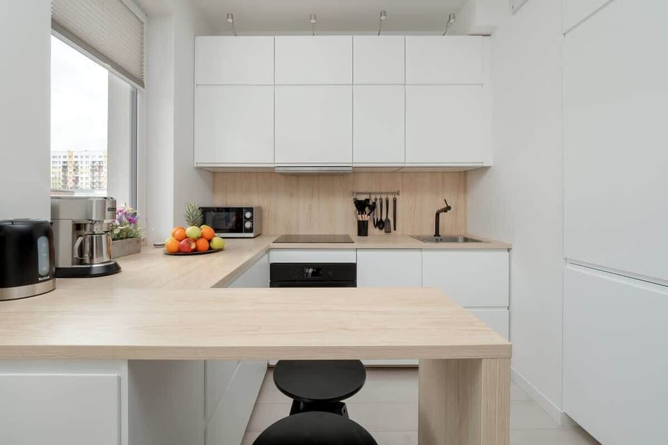A contemporary kitchen featuring white cabinetry, integrated appliances, and vibrant accents like fresh fruit.
