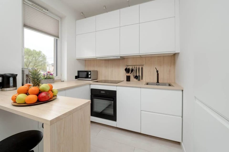 A contemporary kitchen featuring white cabinetry, integrated appliances, and vibrant accents like fresh fruit.
