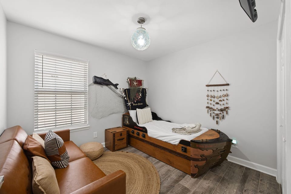 Your imaginative themed bedroom features a unique pirate ship bed with storage details, soft natural light filtering through blinds, a cozy reading chair, and playful decor that makes bedtime an adventure.