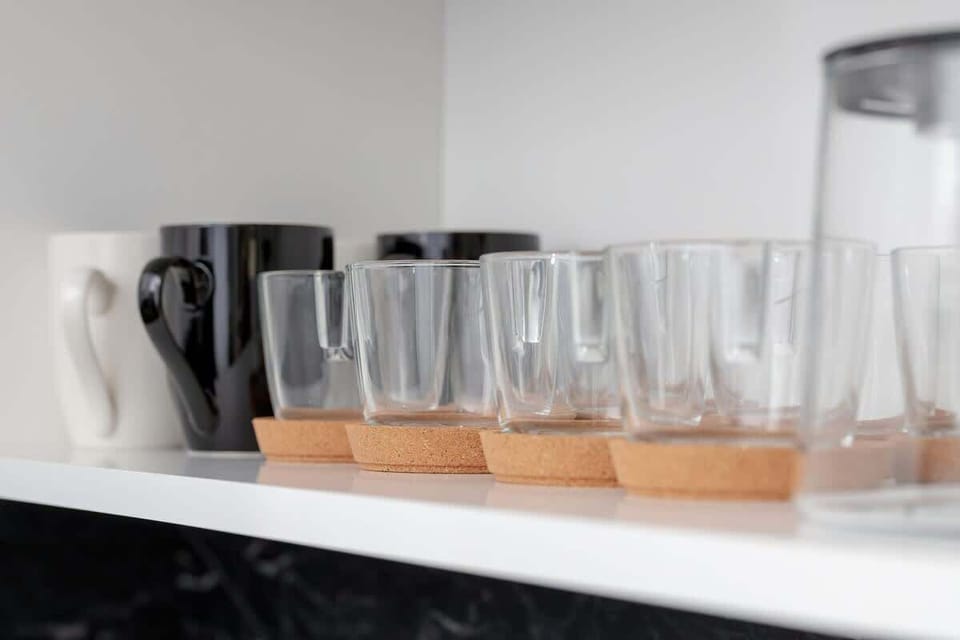 A close-up of a tidy kitchen shelf featuring tall glasses and carafes on a wooden tray.