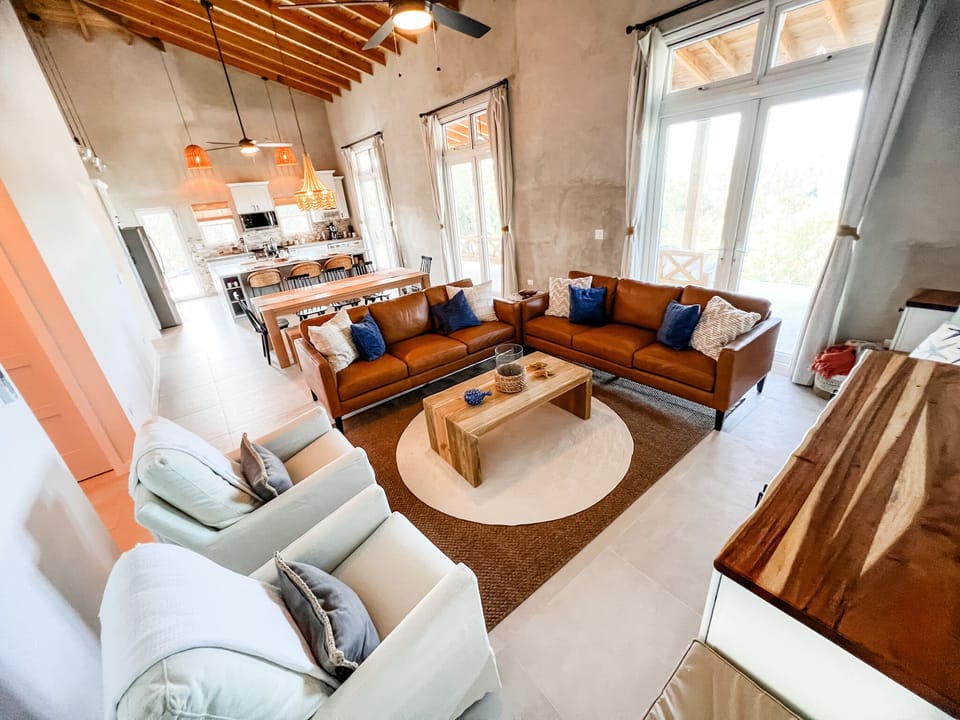 The ocean-view living area features a built-in entertainment center around a 75” smart TV, two large couches, coffee table, comfy swivel glider chairs and window seats.