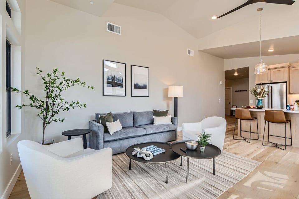 Relax in this bright, airy living room featuring soaring vaulted ceilings and a cozy stone fireplace. Large windows flood the space with natural light, while the open-concept design is perfect for family gatherings.