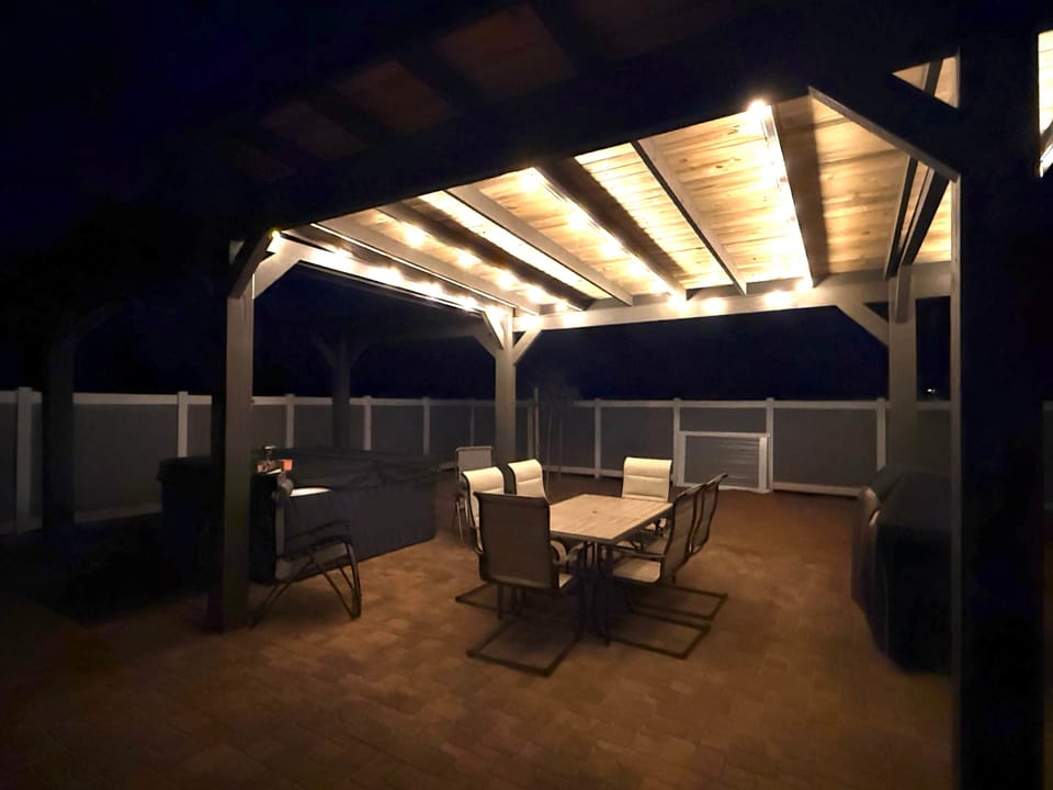 Lighted pergola eating area in private backyard.