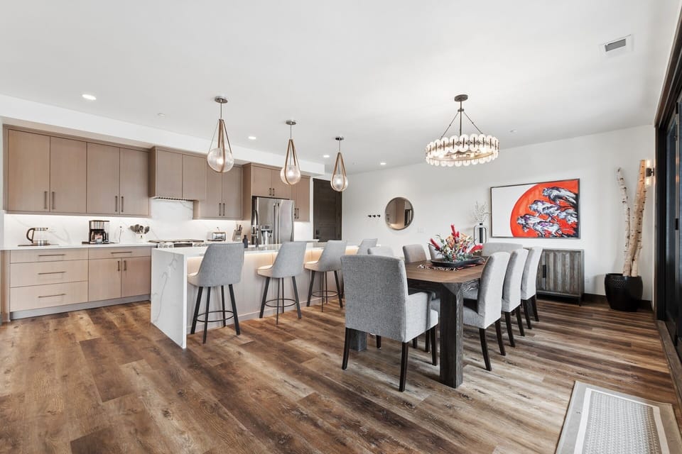 Step into your modern open-plan living space where warm wood floors flow beneath high ceilings. Gather around the large dining table for meals, or perch at the kitchen island bathed in natural light from elegant pendant fixtures.