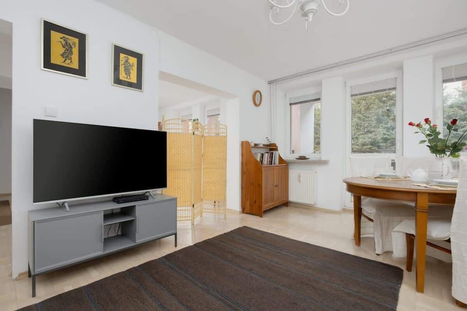 Living room with large TV, wooden cabinets, and dining area.