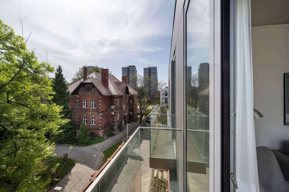 A view from the balcony overlooking a charming red-brick courtyard with trees and architectural details. A peaceful urban escape.