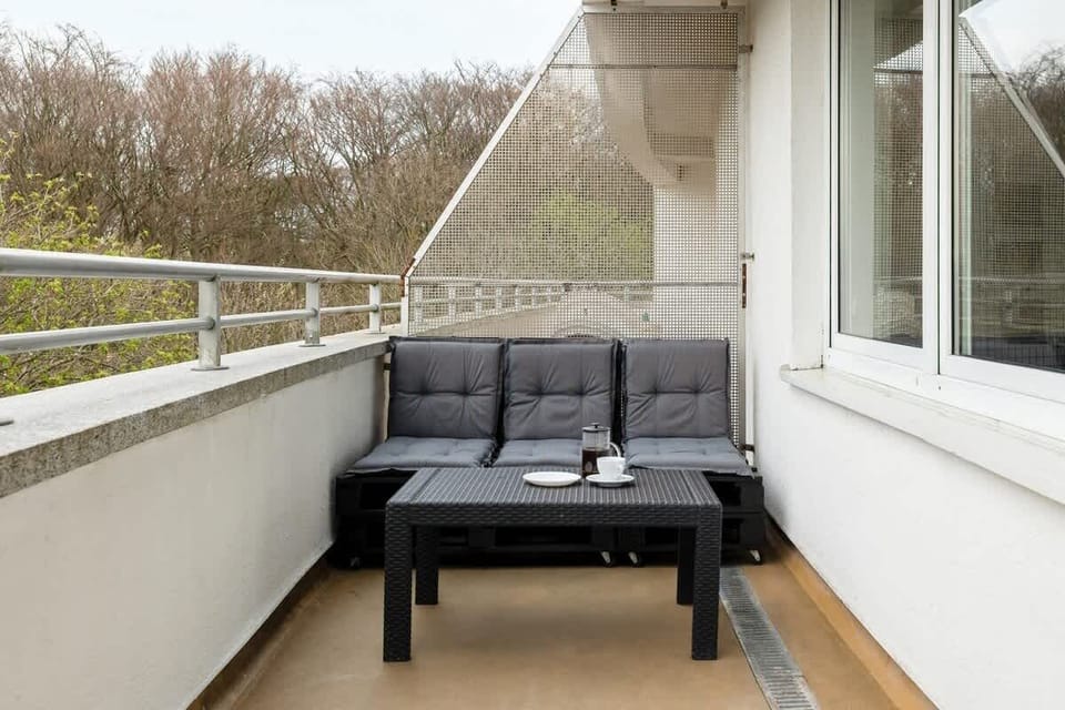 A balcony with a black lounge chair and a view of treetops. Serene and private space.