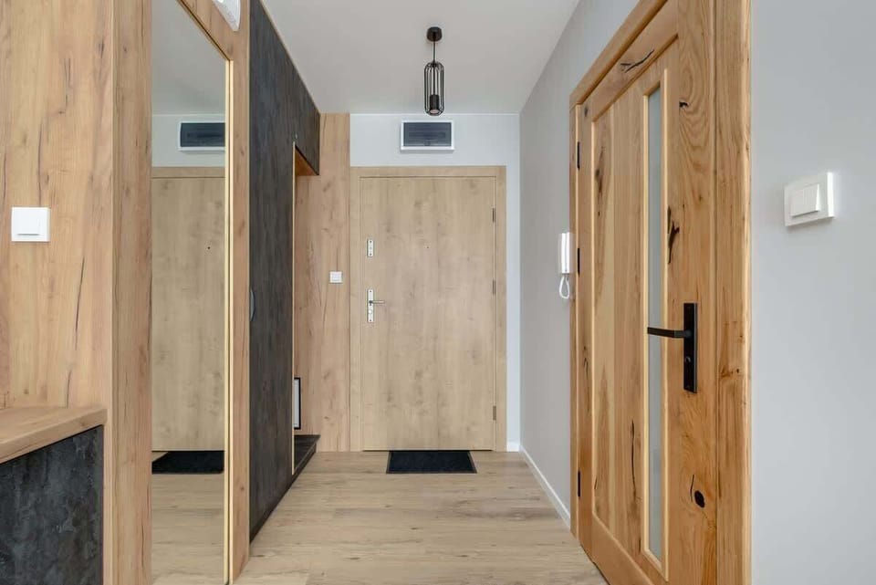 A hallway with wooden closet doors, light flooring, and a mirror on the wall.