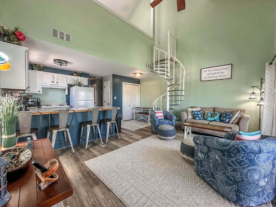 Step into your spacious open-concept retreat where comfort meets coastal charm. Relax on plush seating while the spiral staircase invites upstairs exploration.