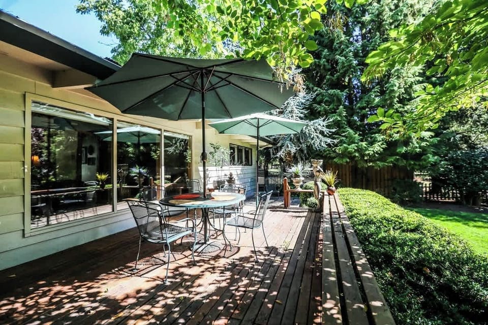 Spacious deck with outdoor dining and seating under large umbrellas—perfect for enjoying a meal, morning coffee, or evening glass of wine while surrounded by trees and fresh air. A cozy spot to relax rain or shine.