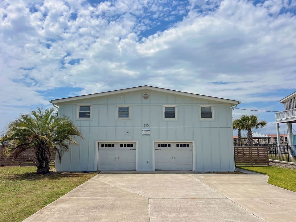 Coastal vacation home features two-car garage parking and inviting light blue exterior with palm trees framing the property, located in a sunny beachside neighborhood.