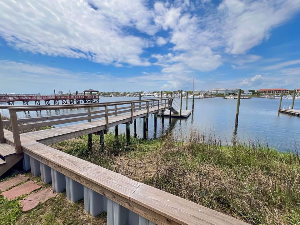 Waterfront property features private dock access along a peaceful marina, with views stretching across calm blue waters to nearby coastal developments under open skies.