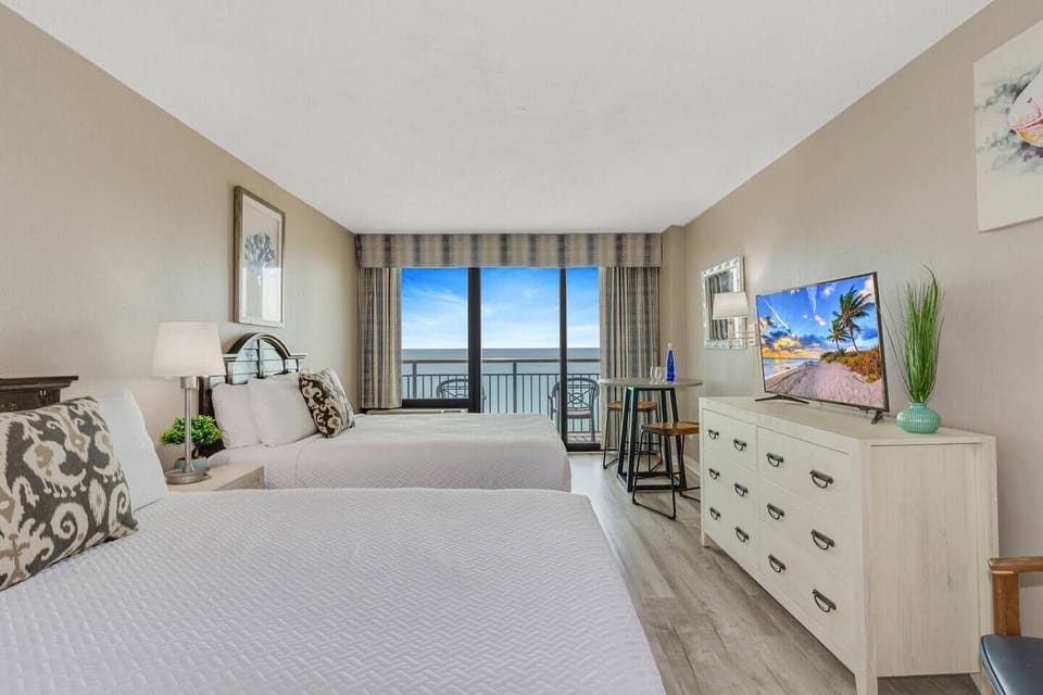 The room has two queen-sized beds and a large sliding glass door that leads to the balcony.