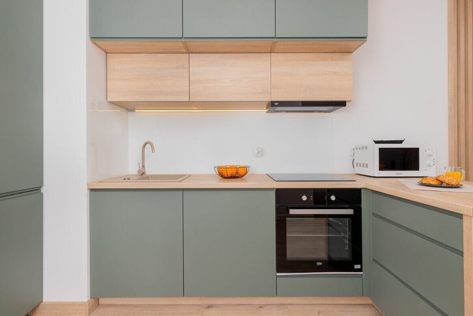 A contemporary kitchen with light grey cabinetry and wooden accents. It includes an oven and ample storage space, designed with clean lines and functionality in mind.