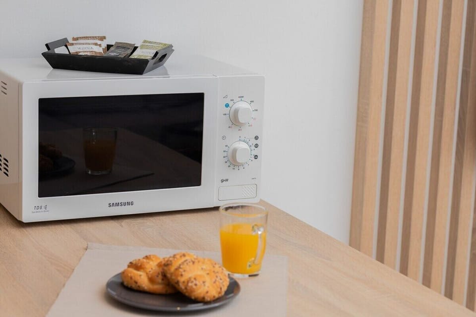 A microwave is displayed on a light wood countertop, alongside a glass of juice and pastries, adding convenience to the kitchen setup.