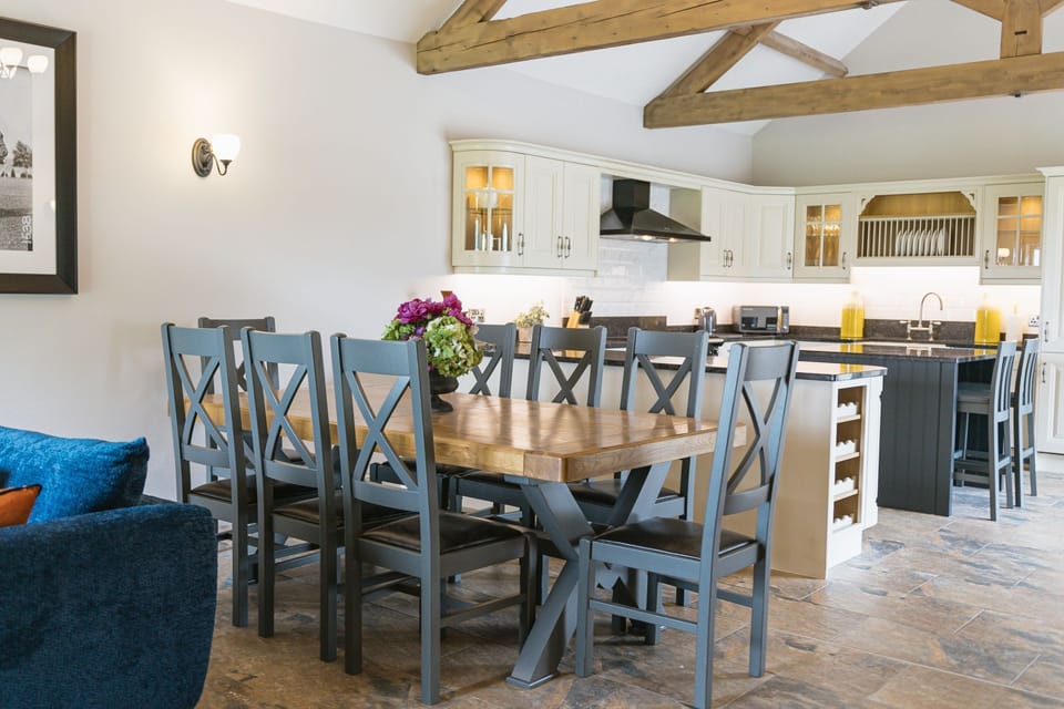 Spacious kitchen diner in Kingfisher cottage with stone flooring and exposed wooden beams.