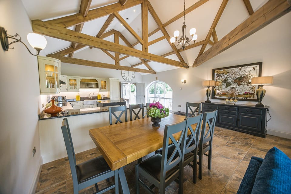 Spacious kitchen diner in Kingfisher cottage with stone flooring and exposed wooden beams.