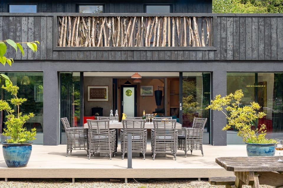 Outdoor dining table on a terrace outside a modern countryside cabin with large glass doors.