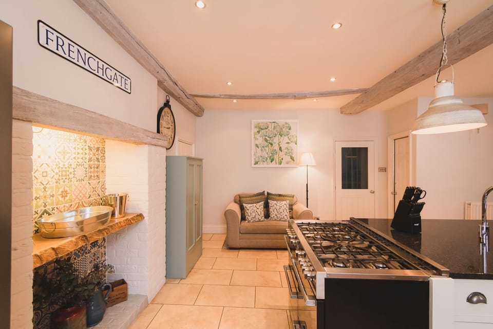 Kitchen at 30 Frenchgate with a range cooker beside the island, pendant lights and exposed beams, plus an inglenook-style alcove with patterned tiles and a small sofa area.
