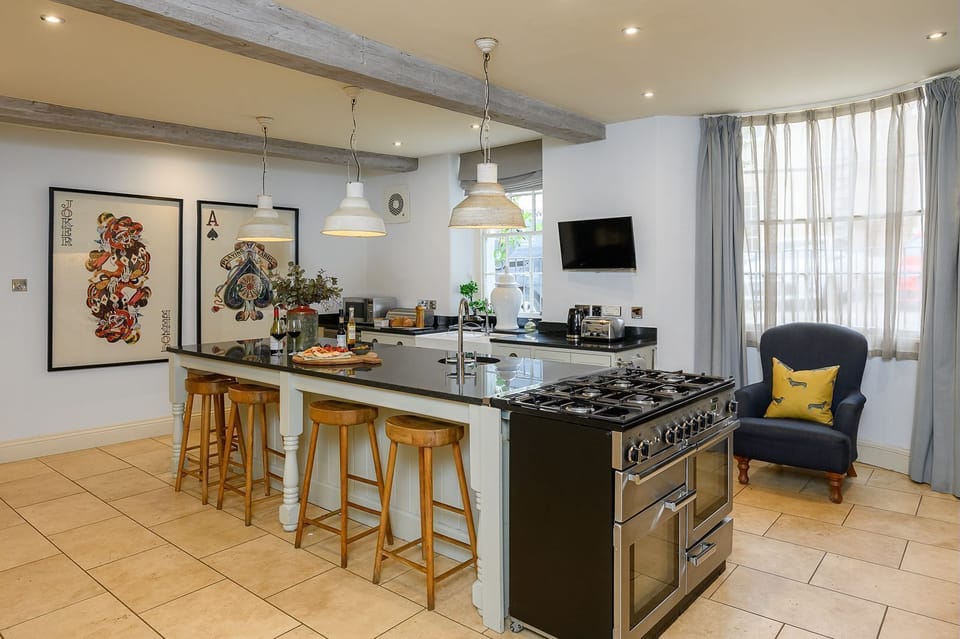Kitchen at 30 Frenchgate with a long island and sink, pendant lights, exposed beams, and an inglenook-style cooker alcove with patterned tiles.