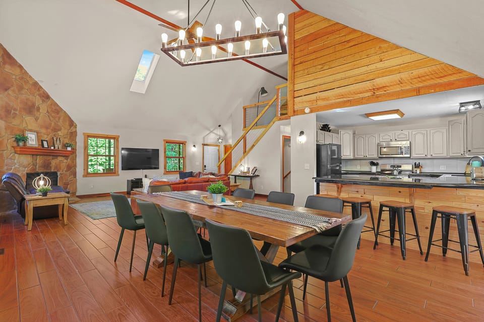 Spacious great room featuring vaulted ceilings, leather seating, a stone fireplace, and beautiful woodland views.