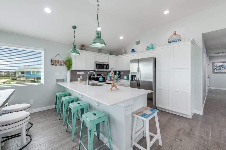 Your coastal-themed kitchen invites culinary adventures with modern stainless appliances, bright white cabinetry, and cheerful turquoise accents throughout.