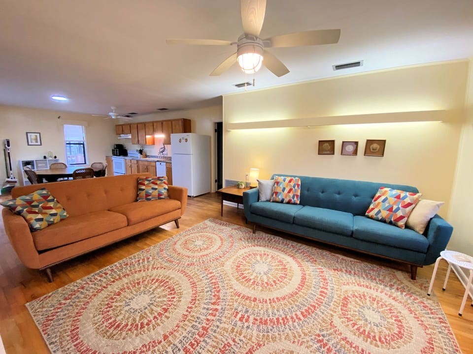 Relax in your stylish living space featuring mid-century modern furniture, colorful geometric pillows, and an open kitchen perfect for home-cooked meals.